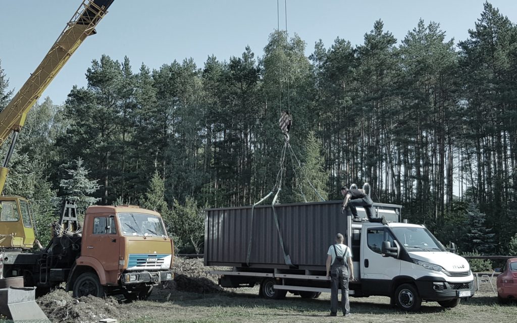Foto eines Krans, der ein mobiles Containerpool von einem LKW in seine endgültige Position transportiert.